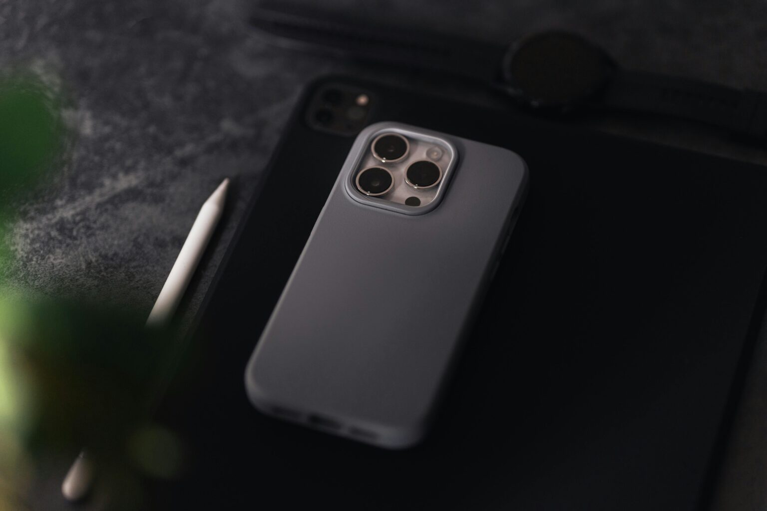 Smartphone, tablet, and smartwatch placed on a dark textured surface with a stylus.